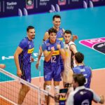 Volleyball players from Finland and Greece competing at the net during a EuroVolley match.